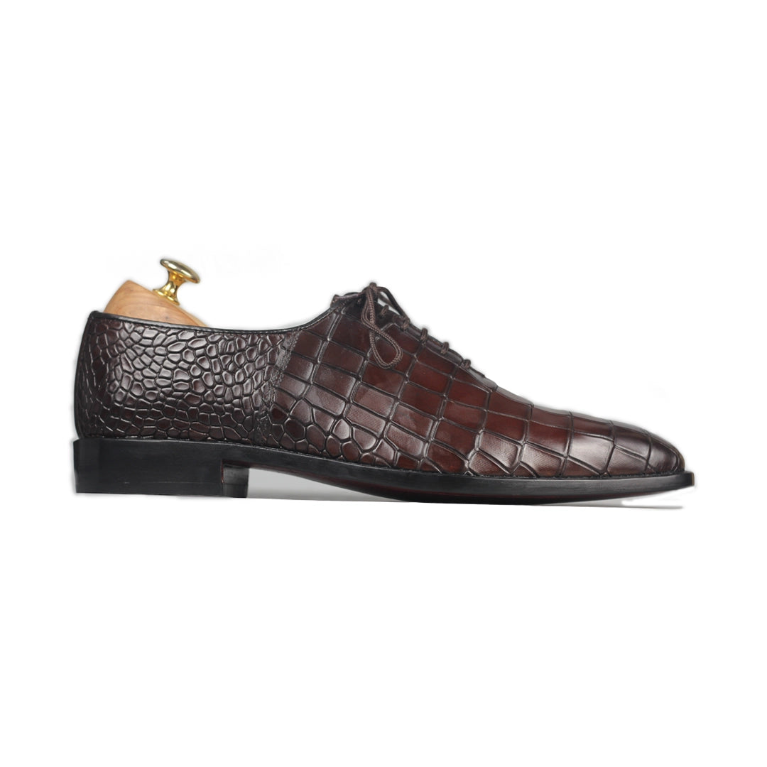 Brown leather shoe with crocodile pattern on a white background