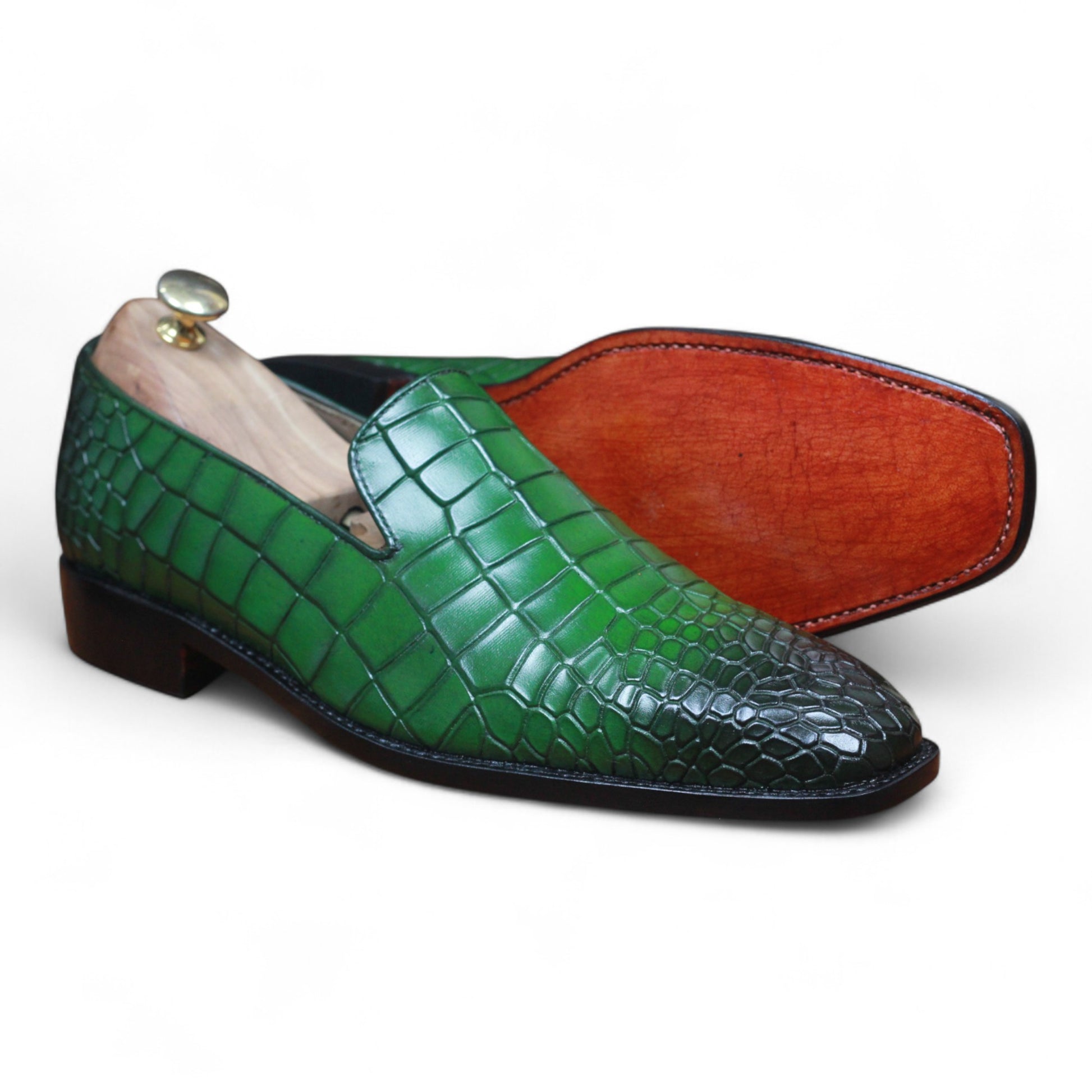 Green textured leather loafers displayed on wooden background

