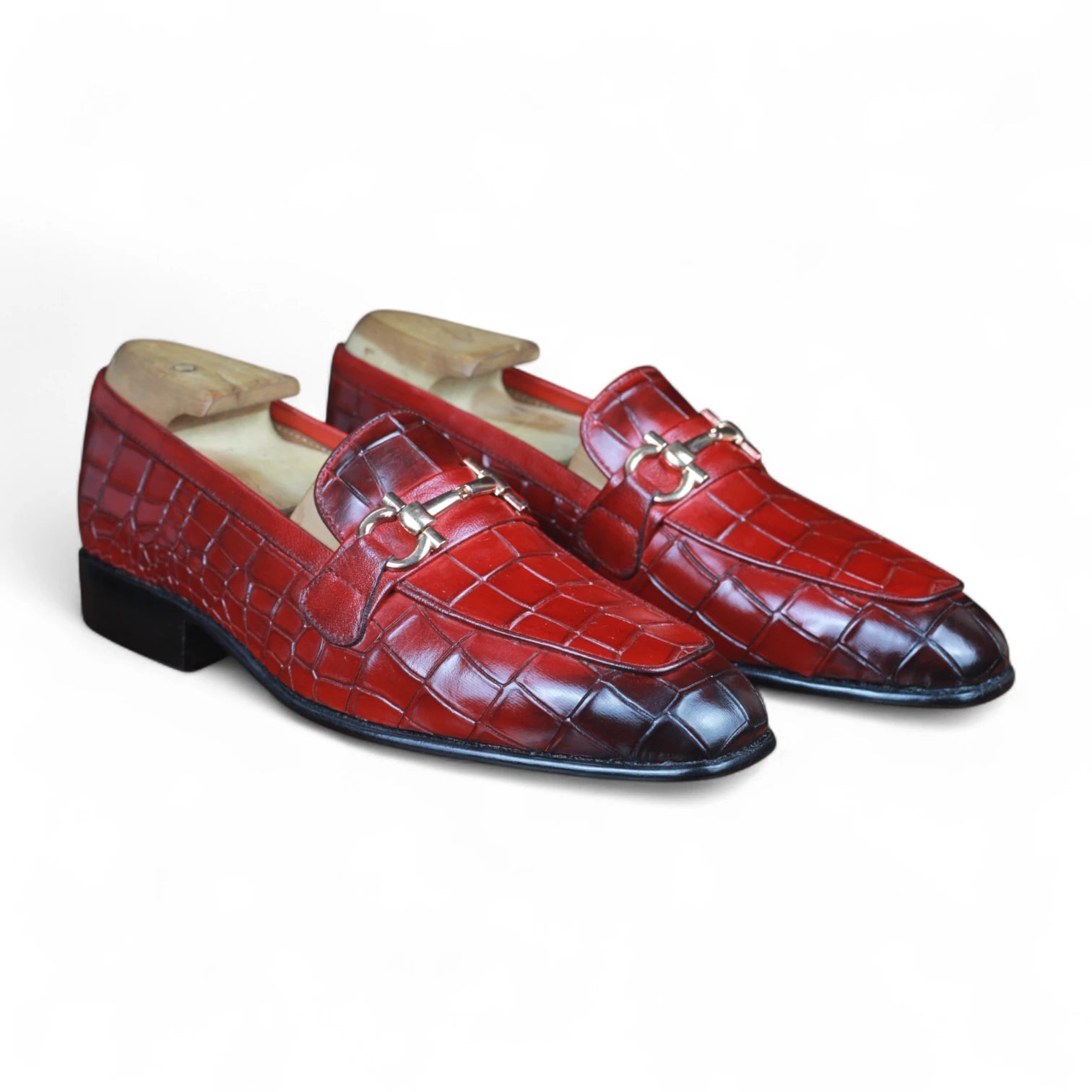 Pair of red crocodile-textured loafers with gold buckles on a white background