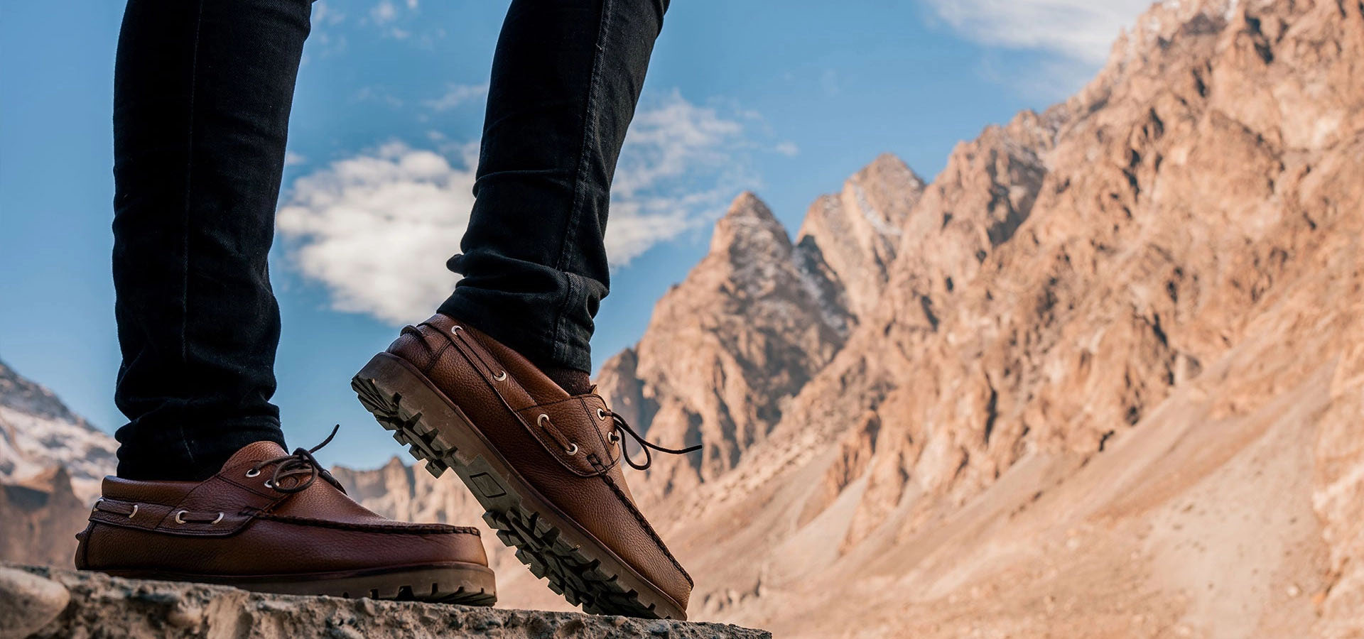 Brown leather shoes worn with dark jeans against a mountainous landscape.1621243260e1af0c20-2