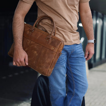 Person holding a brown leather briefcase with a blurred background