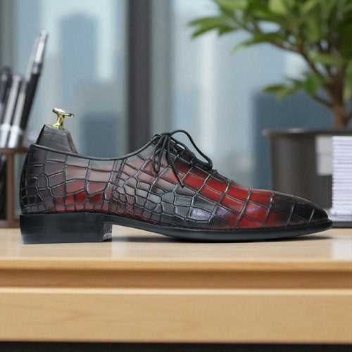 Red and black crocodile-patterned shoe on a wooden surface with a blurred office background